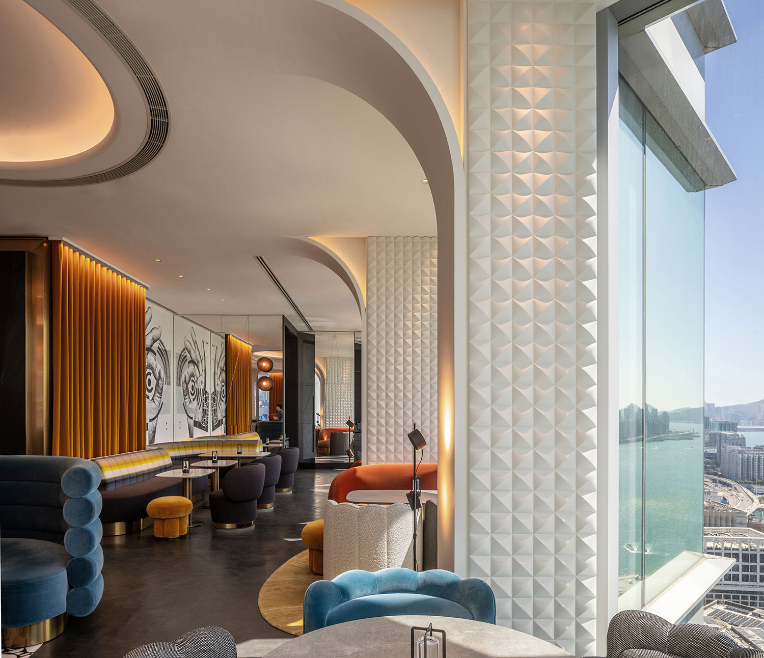 Modern lounge with velvet seating, geometric decor, and a vibrant atmosphere. Large windows reveal a cityscape and river view, creating an elegant ambiance.