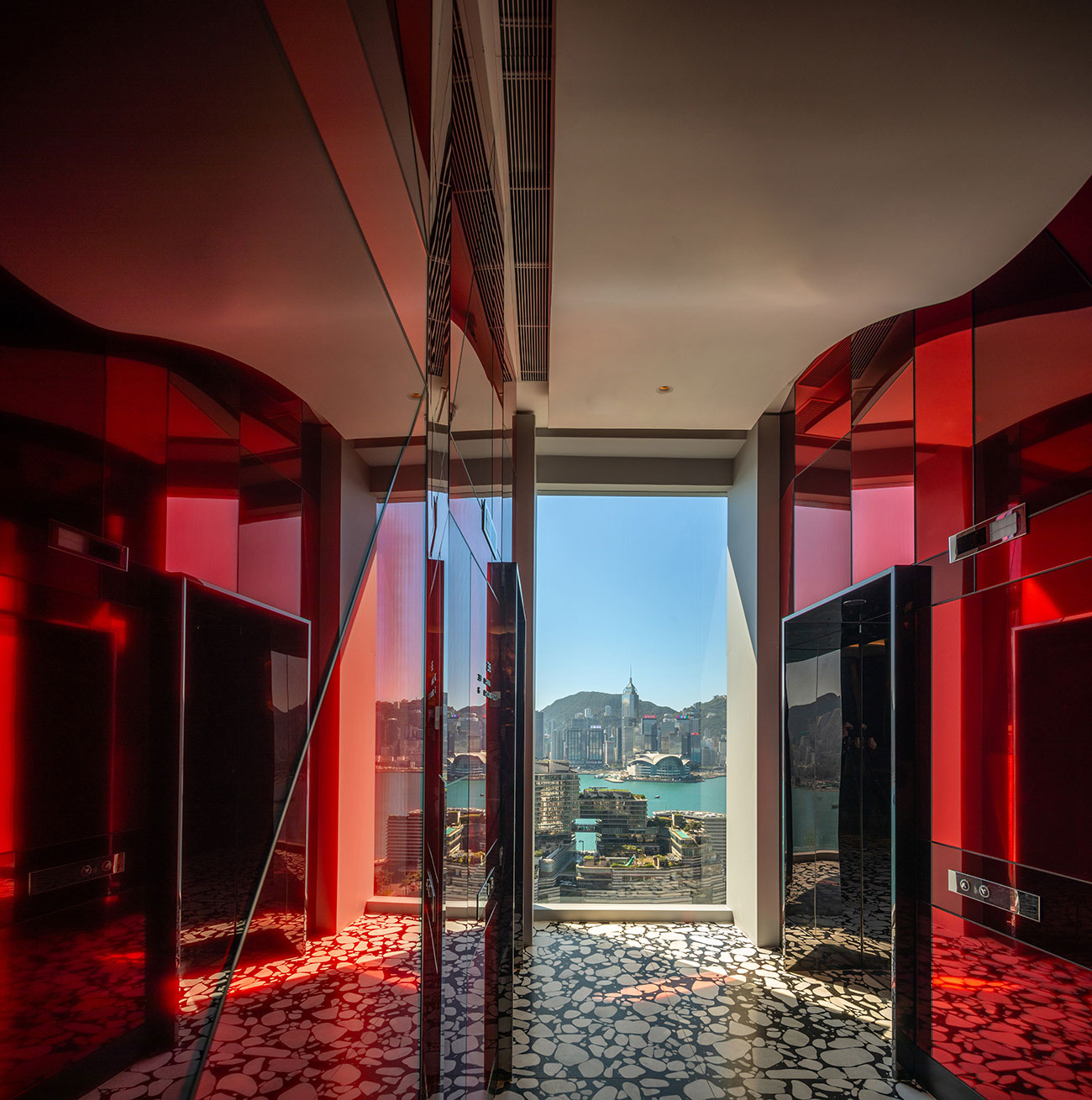 View from a modern corridor with glossy red and black walls, leading to a large window showcasing a cityscape and blue sky. The scene feels vibrant and dynamic.