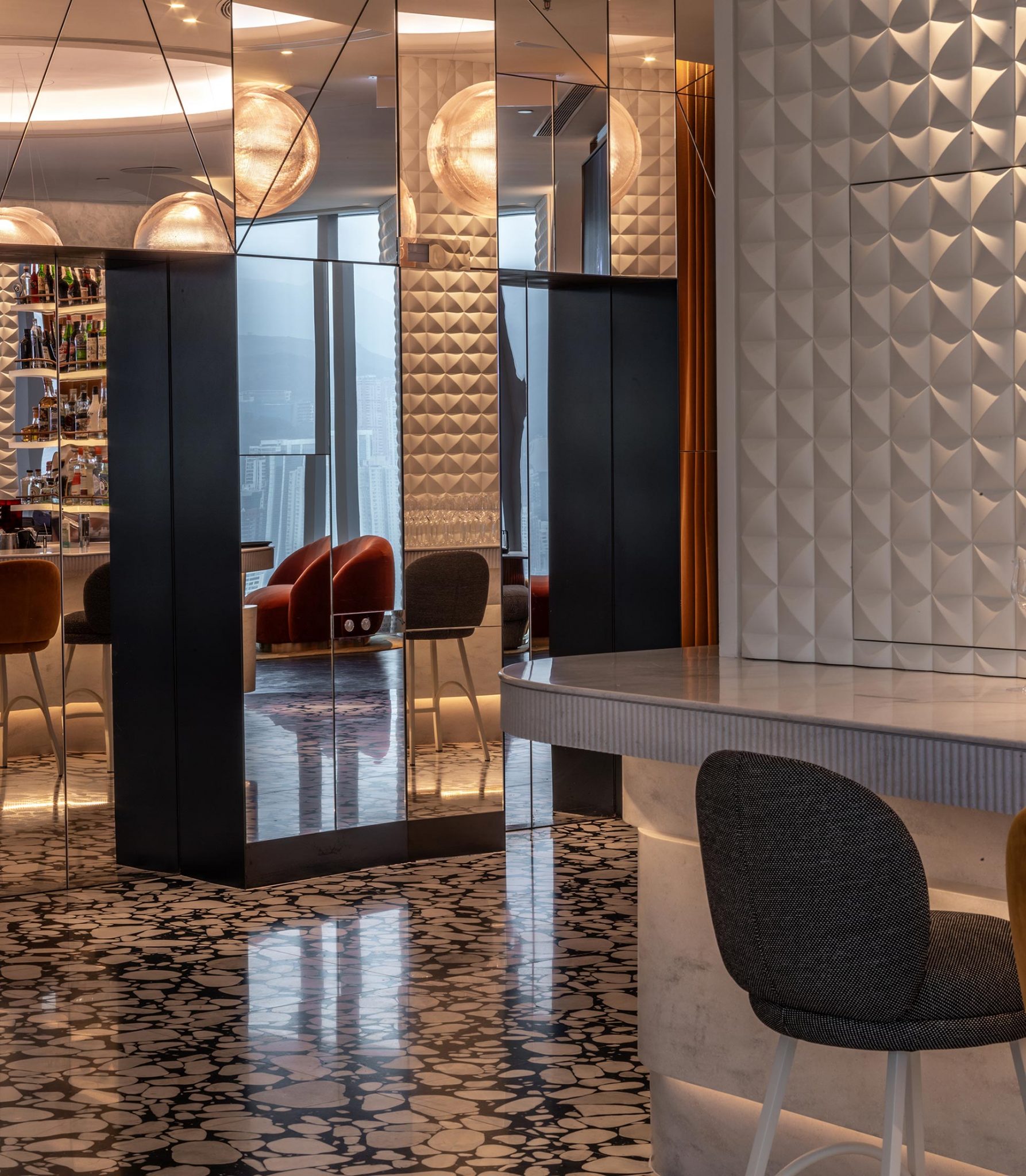 Modern lounge interior with geometric patterns, mirrored walls, and spherical lights. Chairs are arranged near large windows, creating a chic, elegant ambiance.