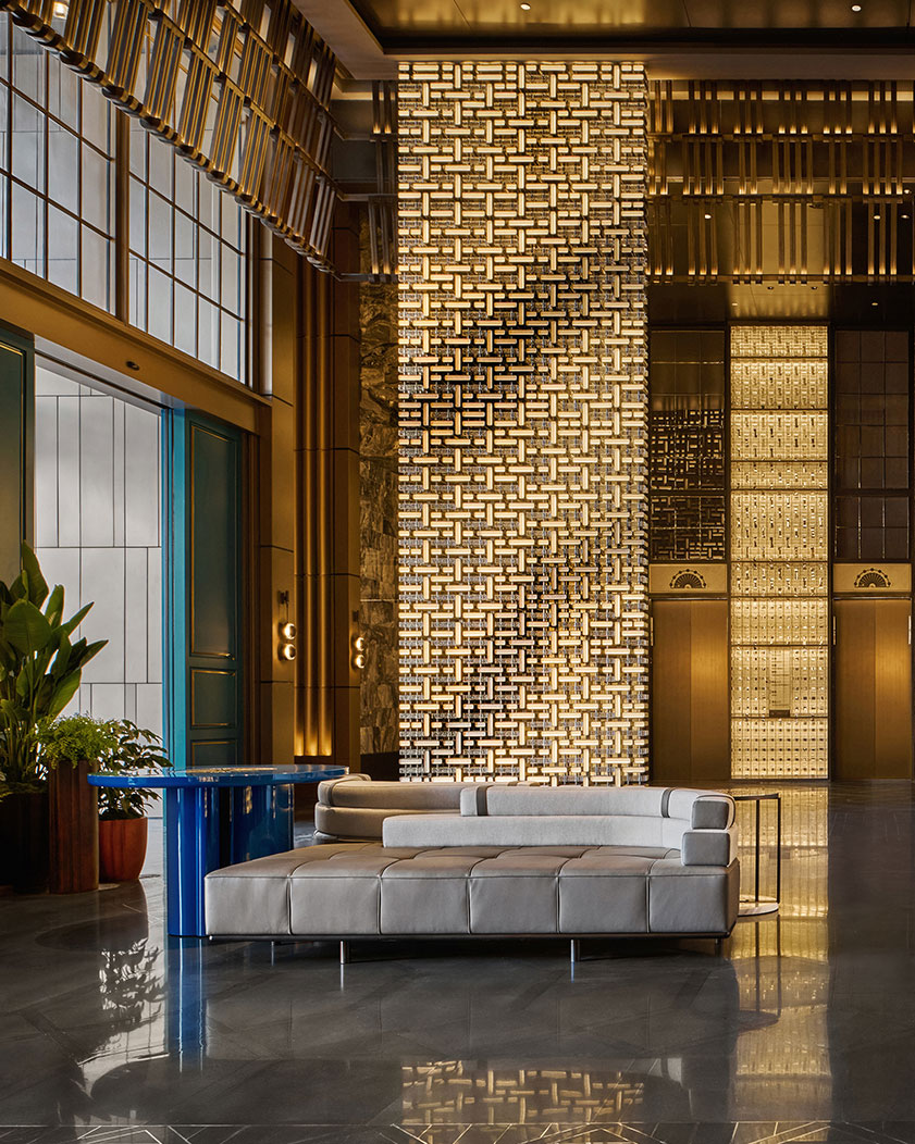 Luxurious hotel lobby features a sleek gray sofa, modern blue-accented table, and a striking, illuminated lattice wall, creating an elegant ambiance.