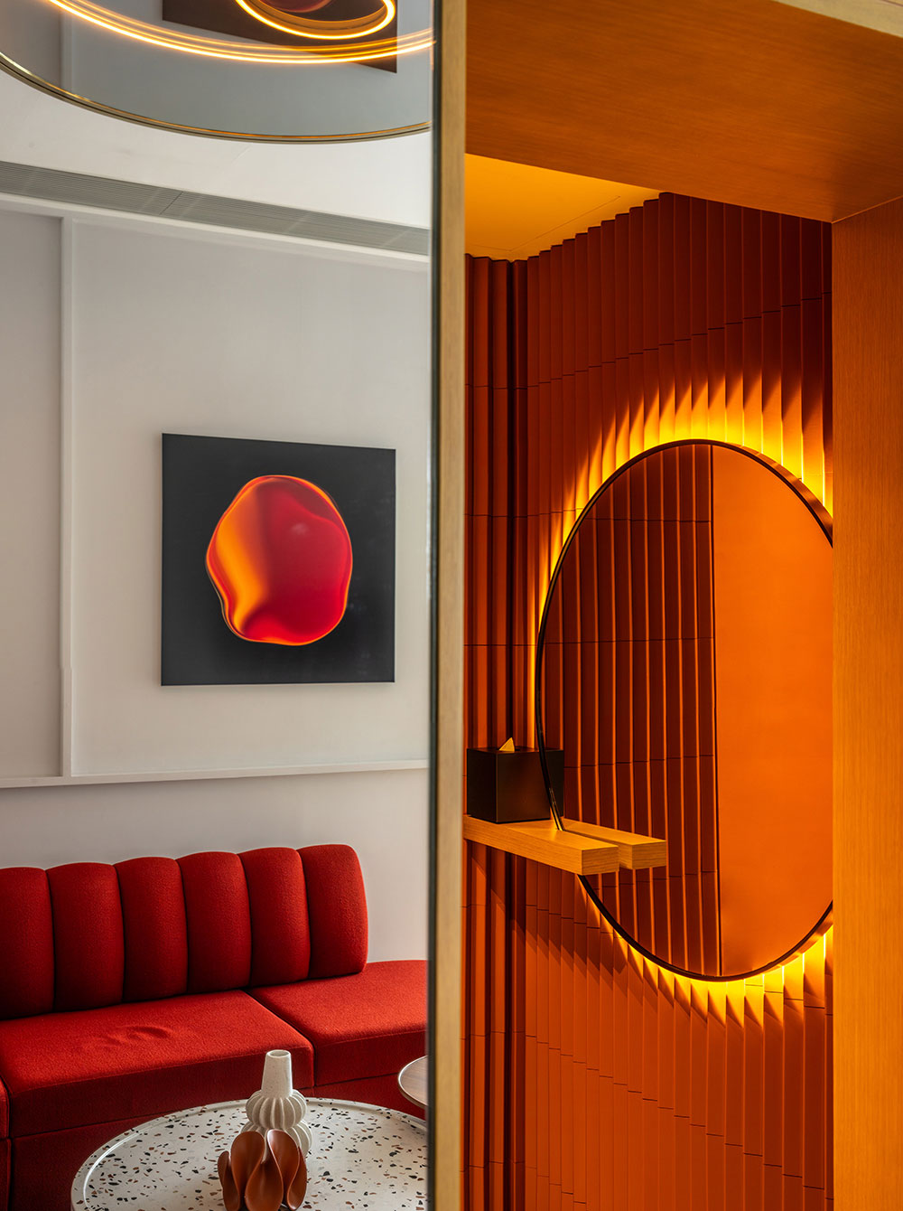 A modern living space with a red sofa, a vibrant abstract wall art, and a terrazzo table. Warm orange lighting creates a cozy, stylish ambiance.