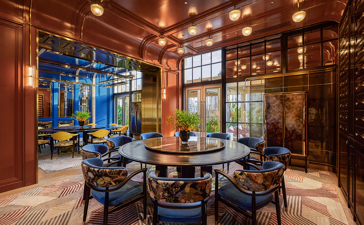 A luxuriously decorated dining room features a round table and plush chairs with floral patterns. Rich blue and gold tones create an elegant ambiance.
