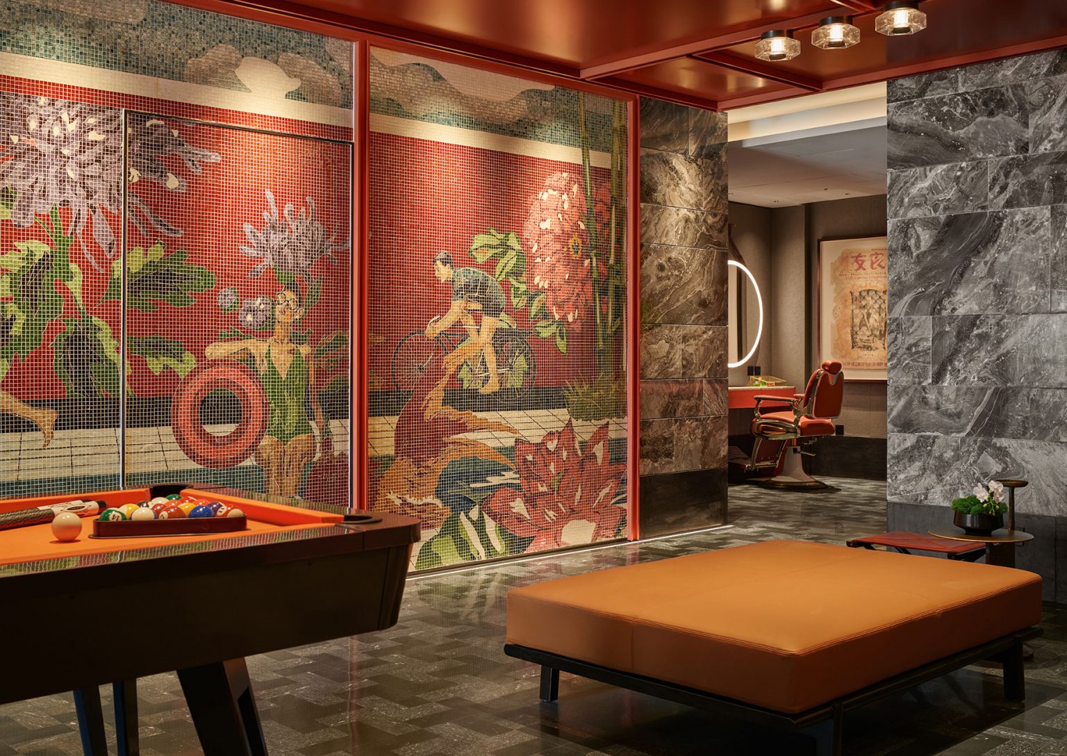 A stylish room with a pool table, vibrant mosaic mural, and plush orange seating. Marble walls and warm lighting create a luxurious, inviting atmosphere.