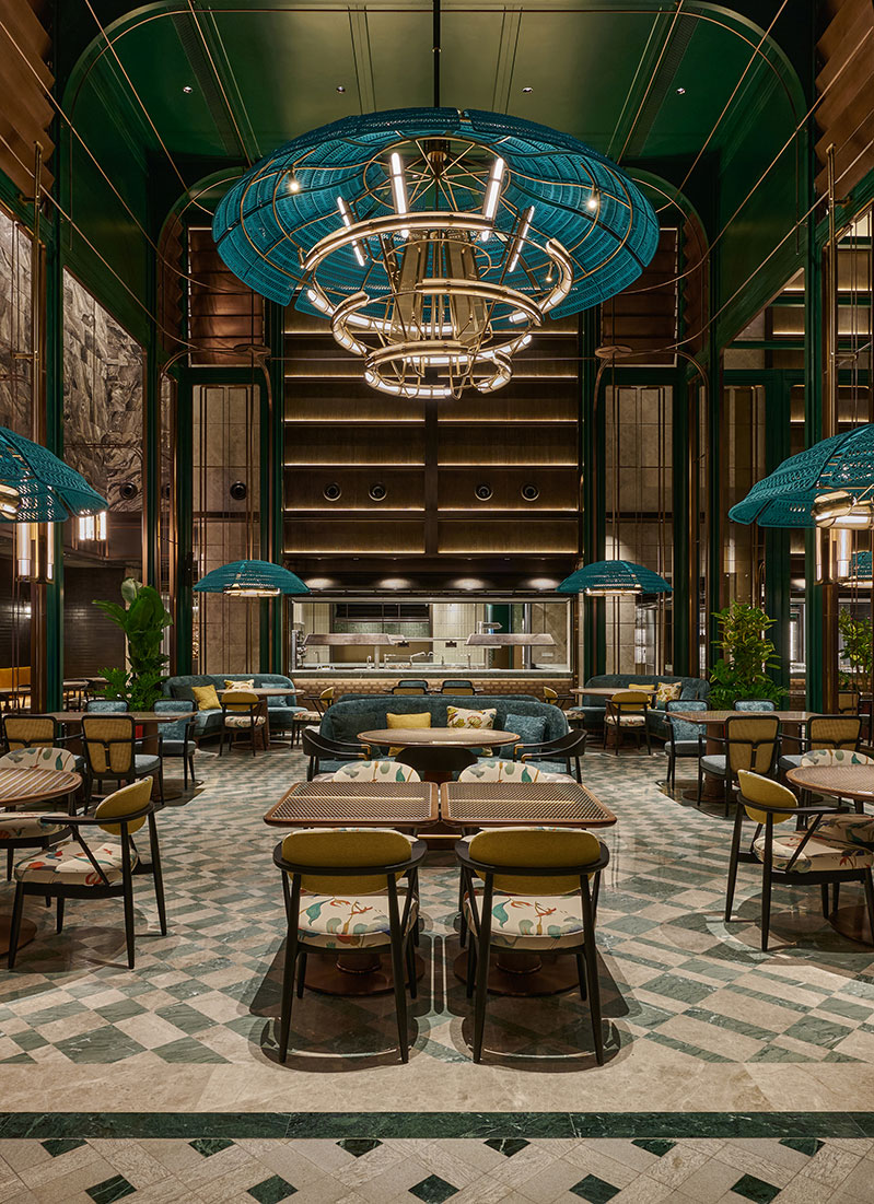 Spacious, elegant restaurant with high ceilings and large blue chandeliers. Greenery surrounds chic seating, creating a cozy, inviting atmosphere.