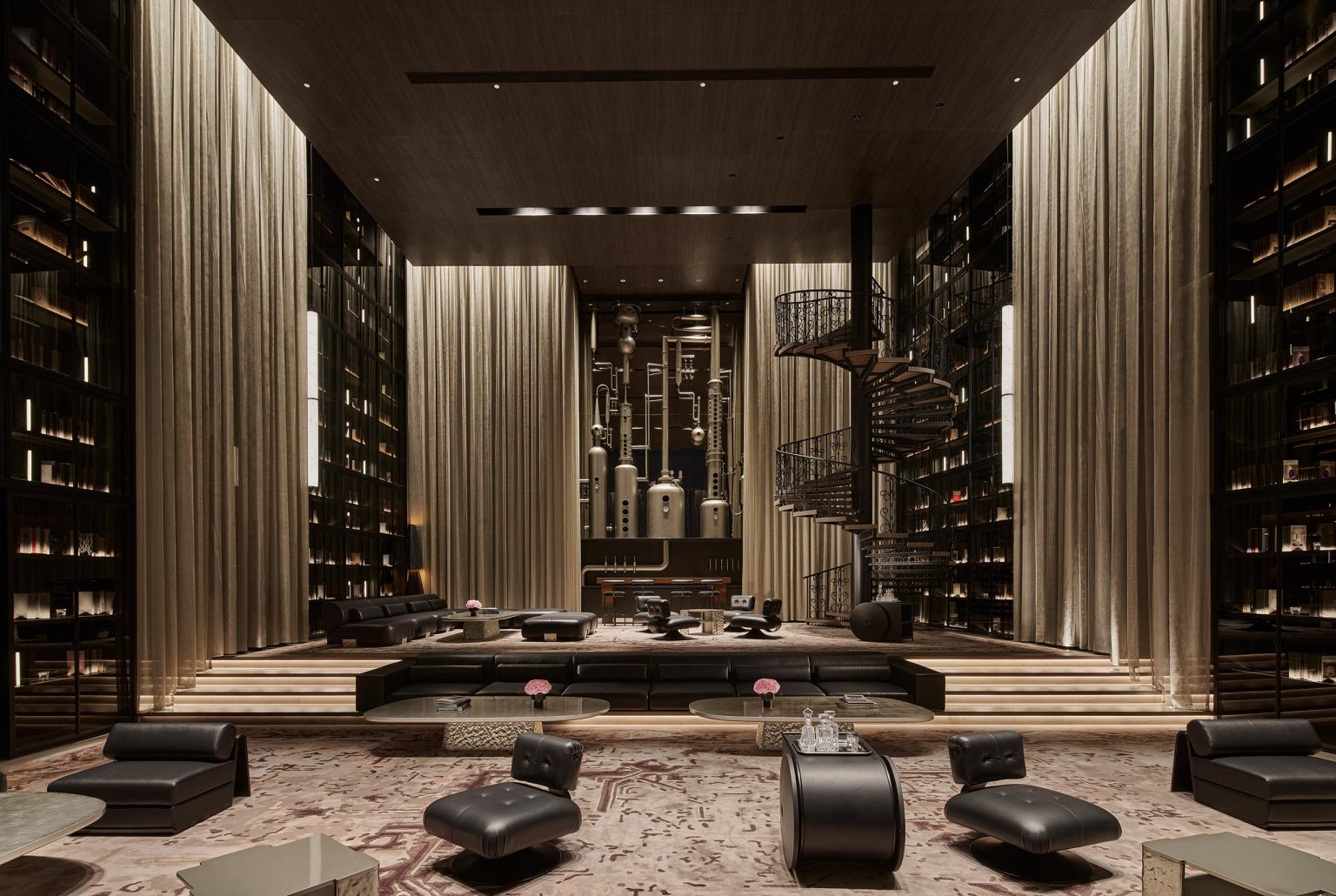 Luxurious hotel lobby with modern decor, featuring tall shelves, elegant spiral staircase, plush seating, and soft ambient lighting creating a sophisticated atmosphere.