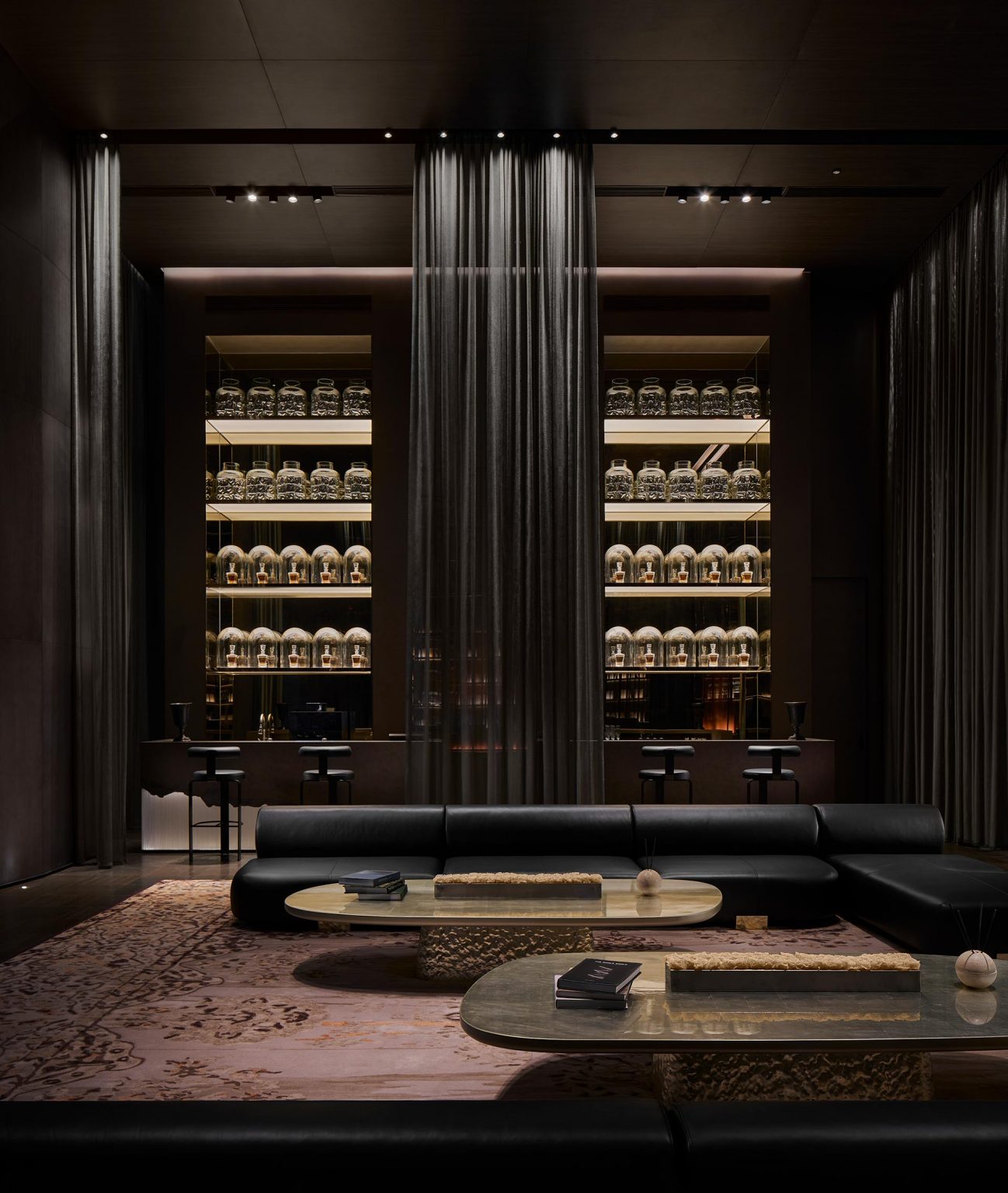 Luxurious lounge with dim lighting, featuring black leather sofas, elegant coffee tables, and backlit shelves filled with jars. Dark, sophisticated ambiance.