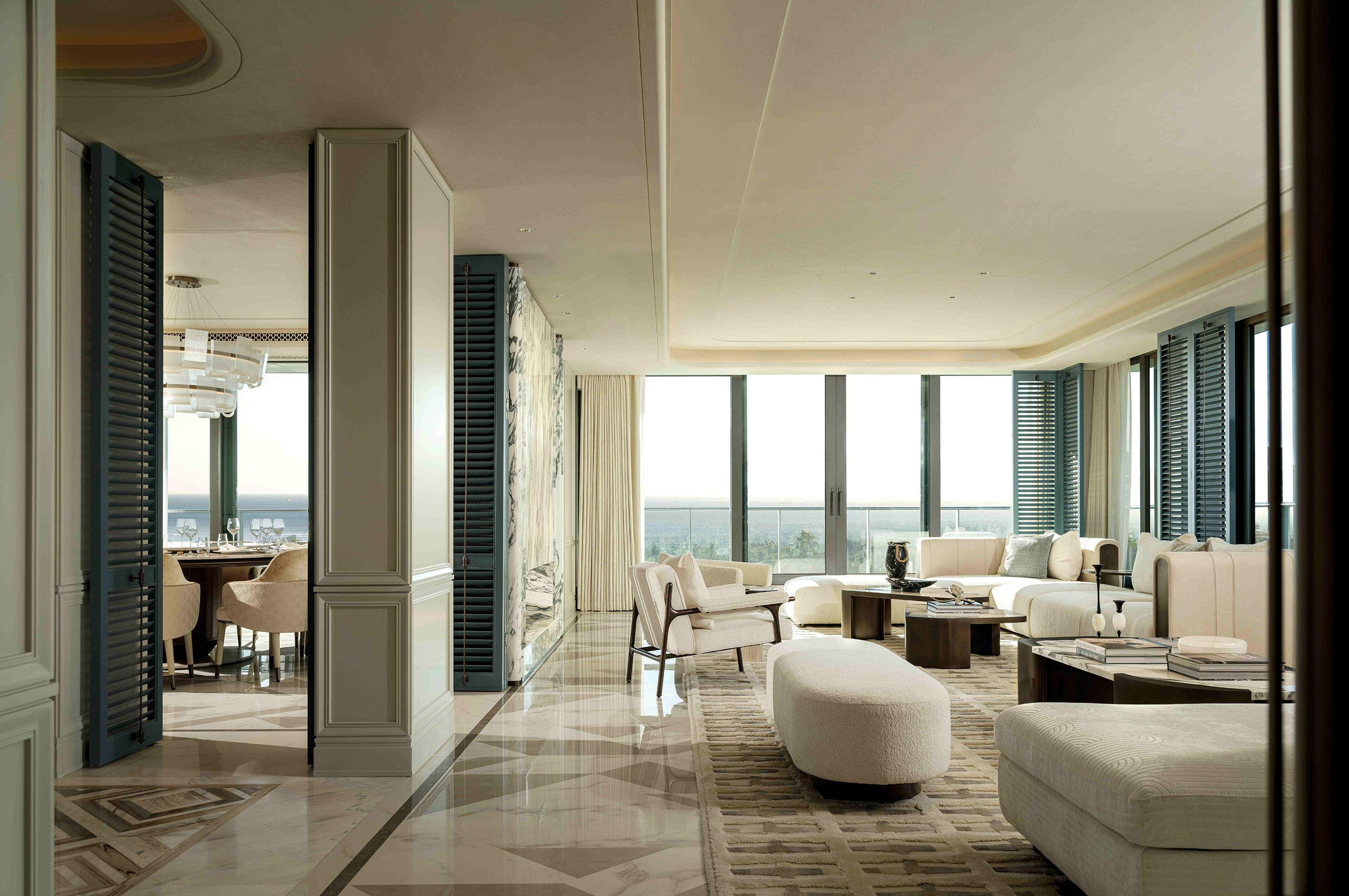 Luxurious modern living room with large windows, plush white sofas, and a neutral color palette. Adjacent dining area adds elegance and warmth.