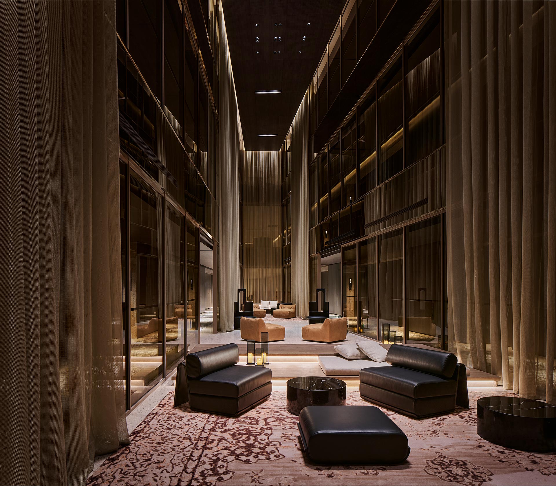 Luxurious hotel lobby with high ceilings, soft lighting, and elegant decor. Black leather seating and warm-toned rugs create a cozy, sophisticated atmosphere.