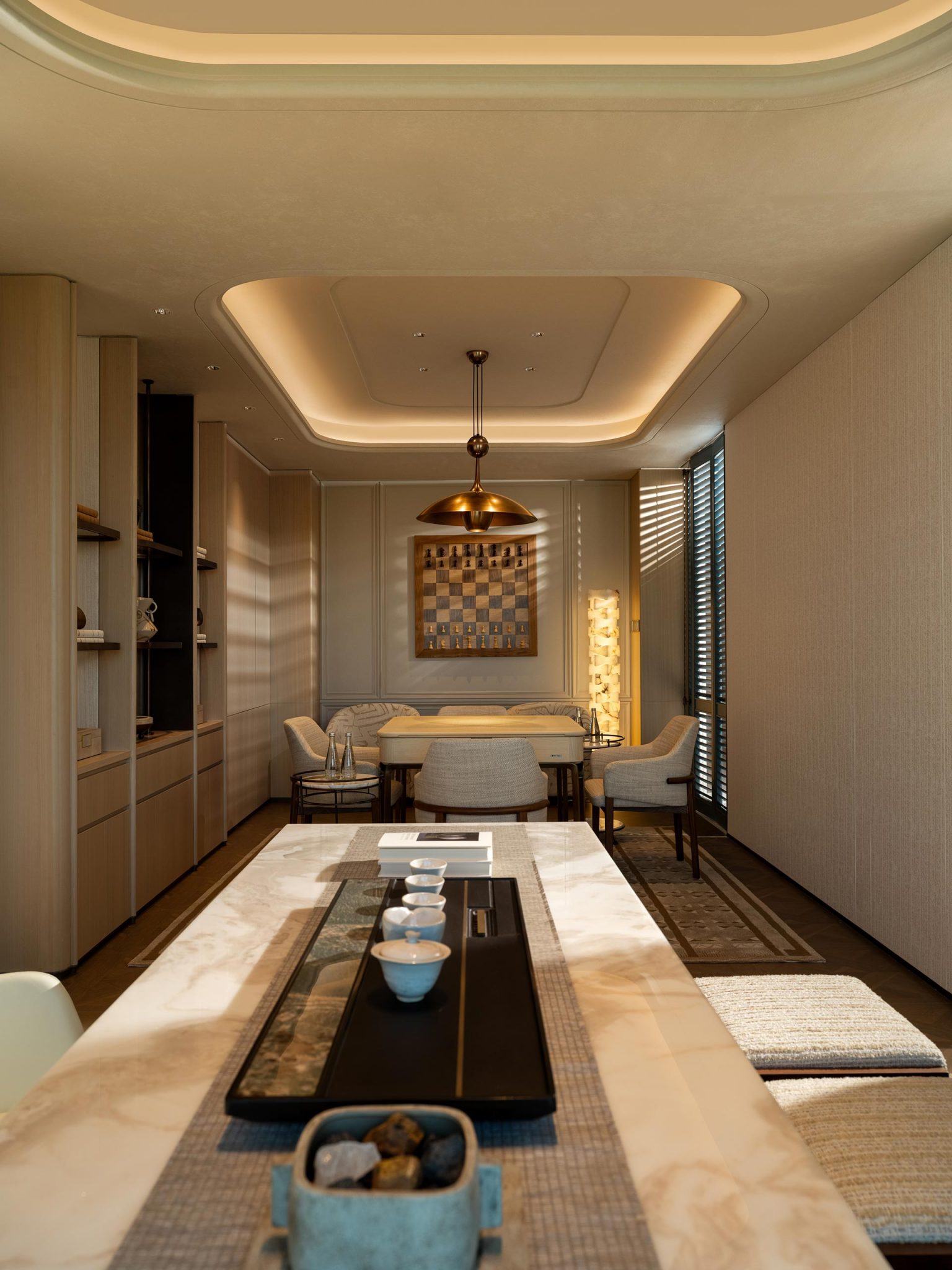 Modern dining room with a long marble table, elegant chairs, and ambient lighting. A decorative art piece and tall lamp add warmth and style.