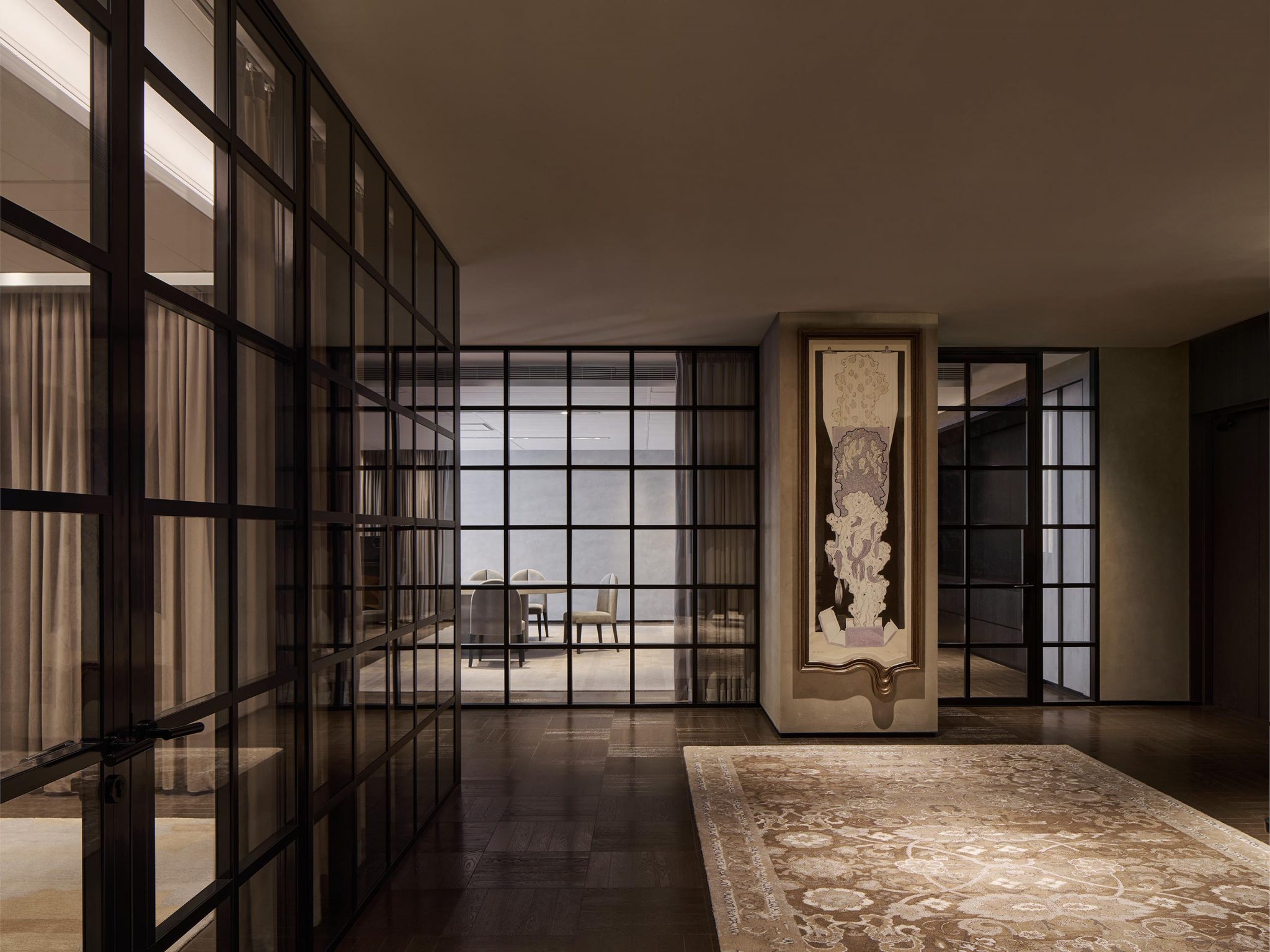 Modern interior with glass-paneled walls and a large ornate rug. A framed abstract art piece is prominently displayed, creating an elegant ambiance.