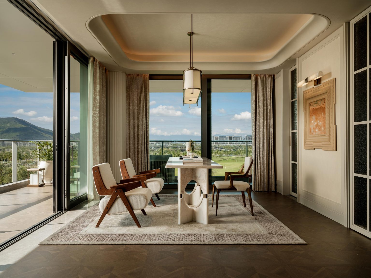 Elegant dining room with vintage chairs around a marble table on a plush rug. Large windows offer a scenic view of mountains and a sunny sky. Modern decor.