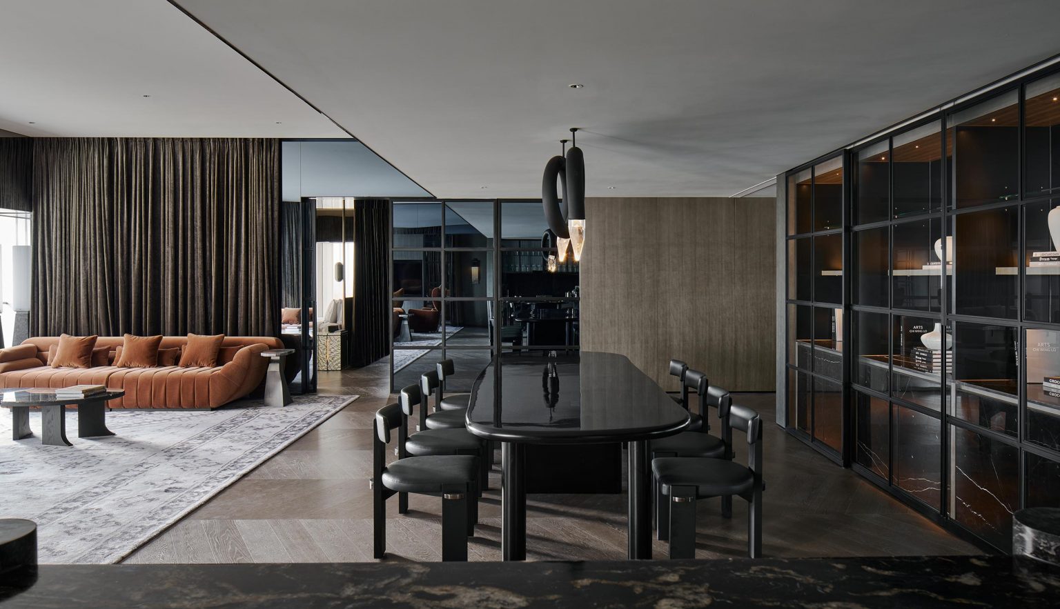 Modern open-plan living and dining area with a brown leather sofa, black dining table and chairs, glass cabinets, and neutral-toned decor.