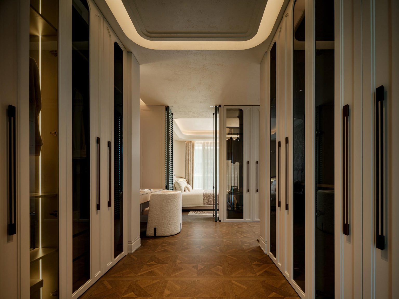 A luxurious walk-in closet with dark wood floors and mirrored wardrobe doors leads to a softly lit bedroom. The space is modern and elegant.