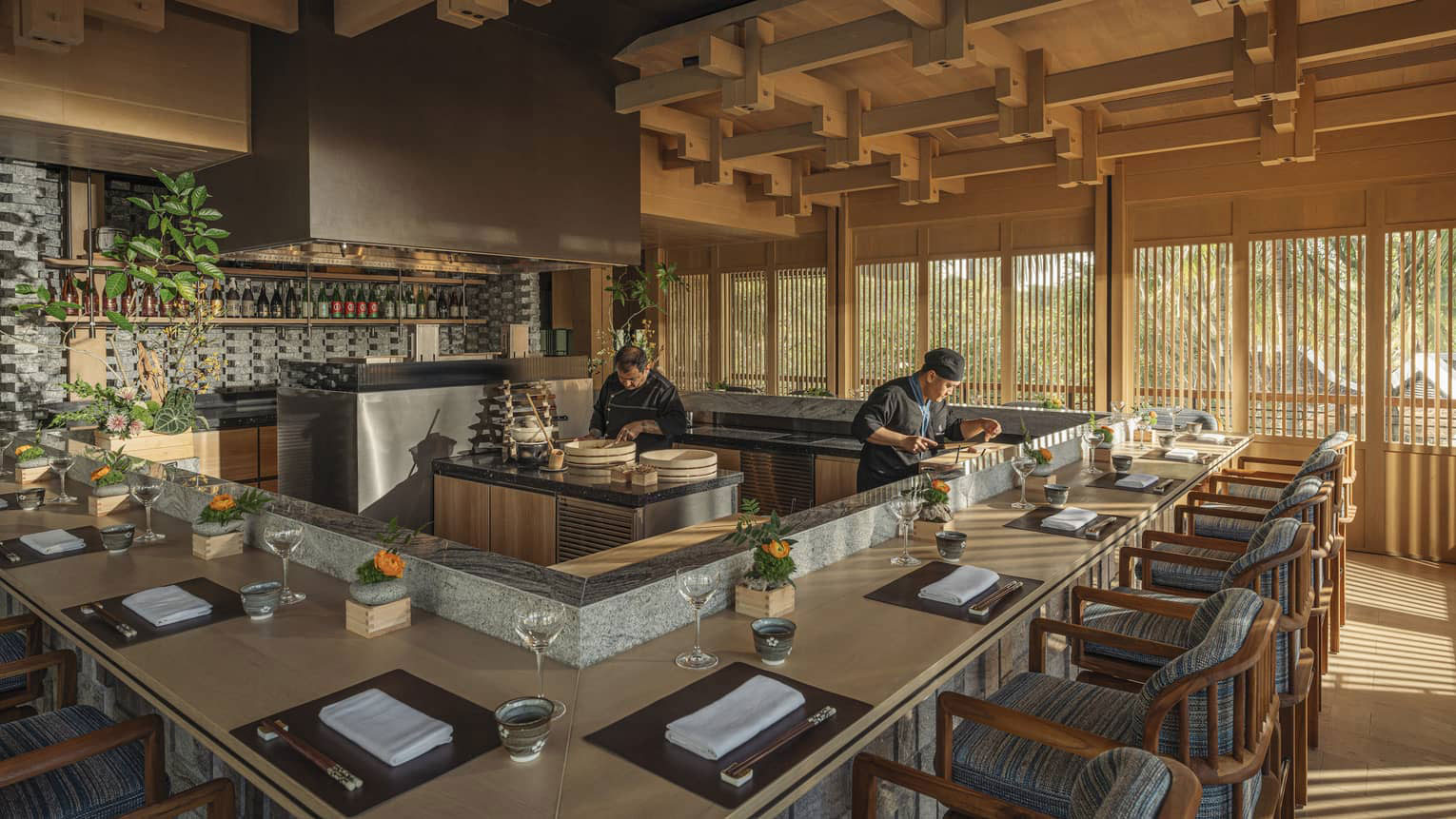 Chefs preparing food behind a sleek, U-shaped wooden omakase dining counter with neatly set place settings under a modern wooden lattice ceiling.