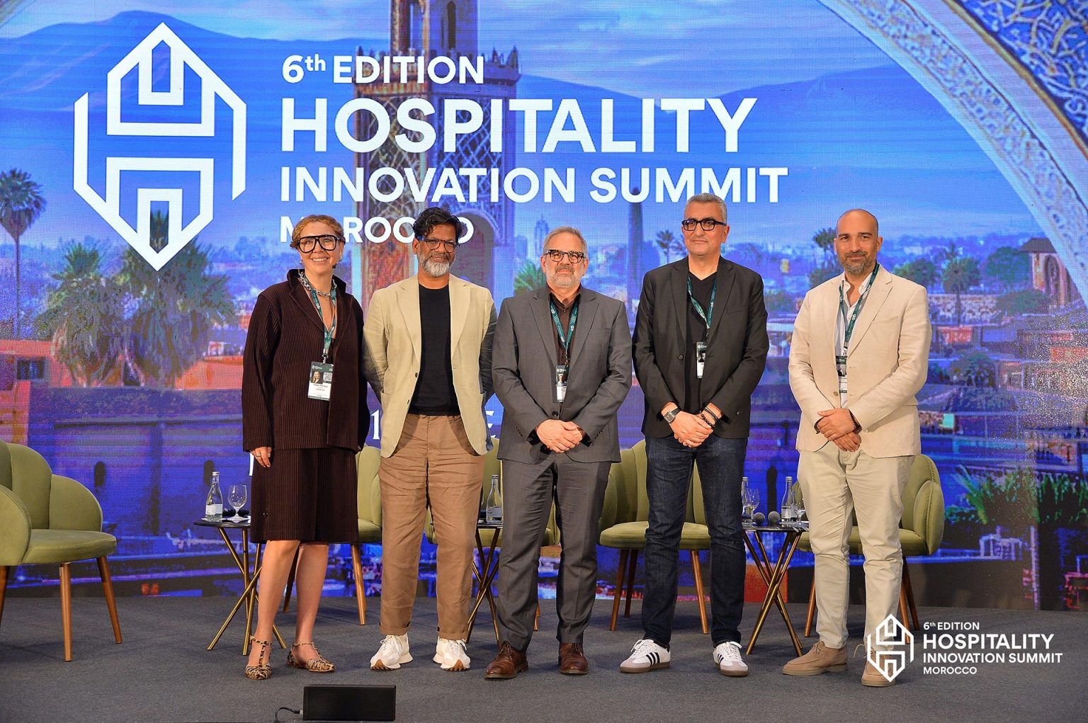 Five individuals stand on a stage at the 6th Edition Hospitality Innovation Summit in Morocco, smiling confidently in business attire against a vibrant backdrop.